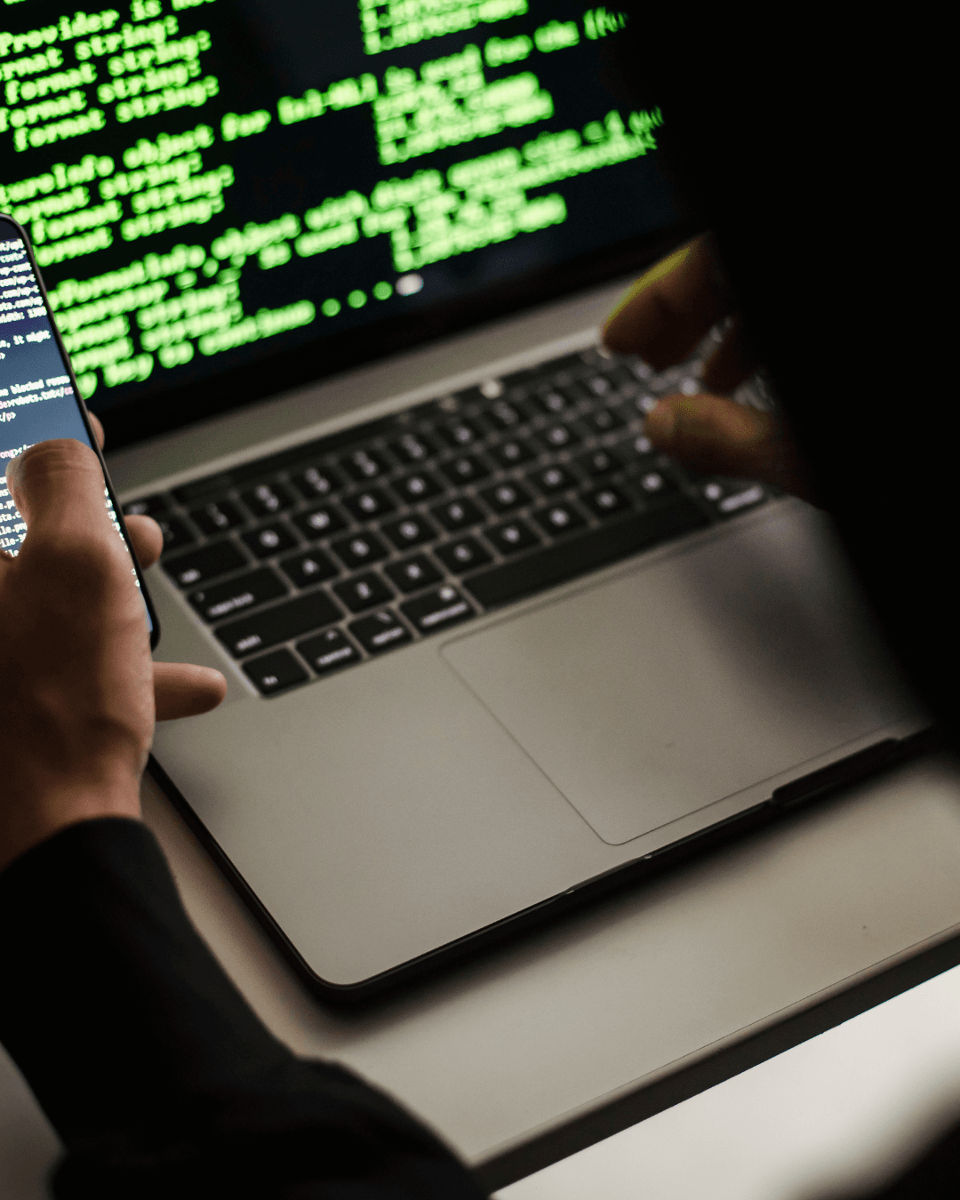Hands typing on a laptop beside a phone showing code